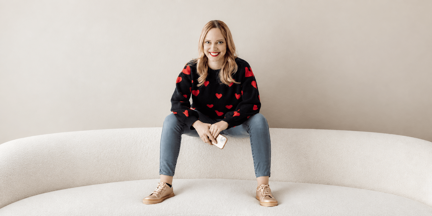 Woman with long blonde hair in a heart-patterned sweater sitting on a couch