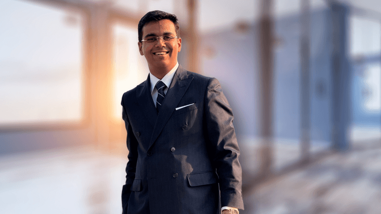 The image features Vibhaas Singh, the visionary behind Hemco, wearing a formal suit and standing confidently in a modern office setting, symbolizing innovation and leadership in kitchen technology.