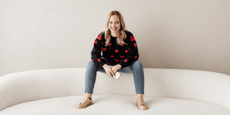 Woman with long blonde hair in a heart-patterned sweater sitting on a couch