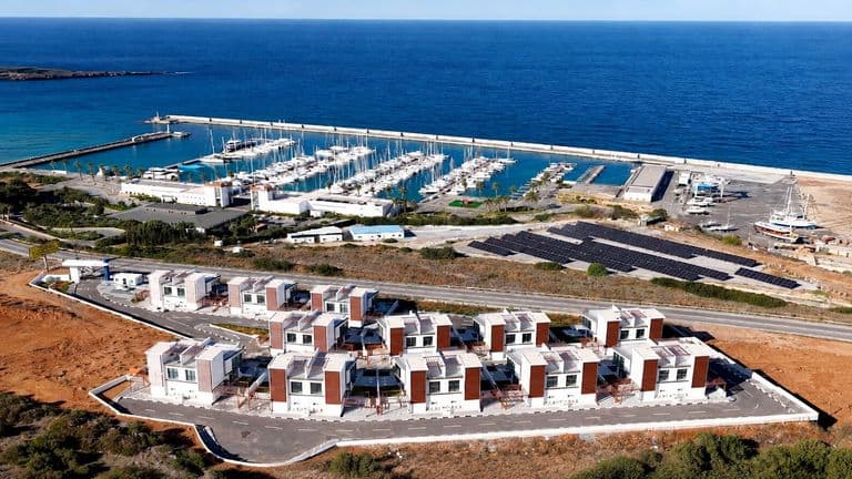 Aerial view of modern coastal homes beside a marina filled with yachts and the Mediterranean Sea.