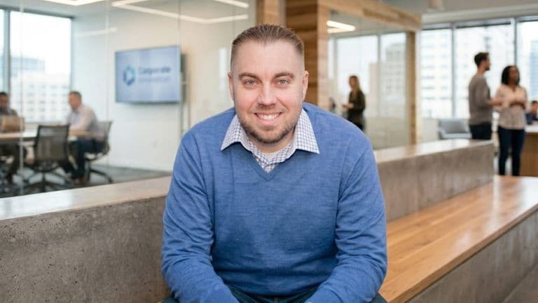 Professional realtor smiling in modern office, coworkers blurred in background, bright corporate workspace.