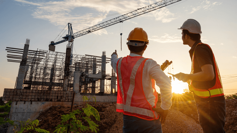 Construction workers in safety vests inspect a residential building site with a tower crane at sunset.