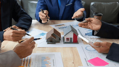 Group of people discussing real estate models and charts at a meeting table