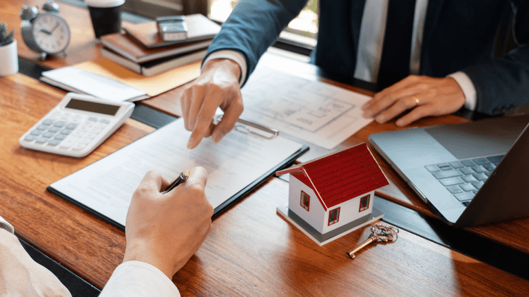 Two businesspeople discussing paperwork with a miniature house and calculator on the table