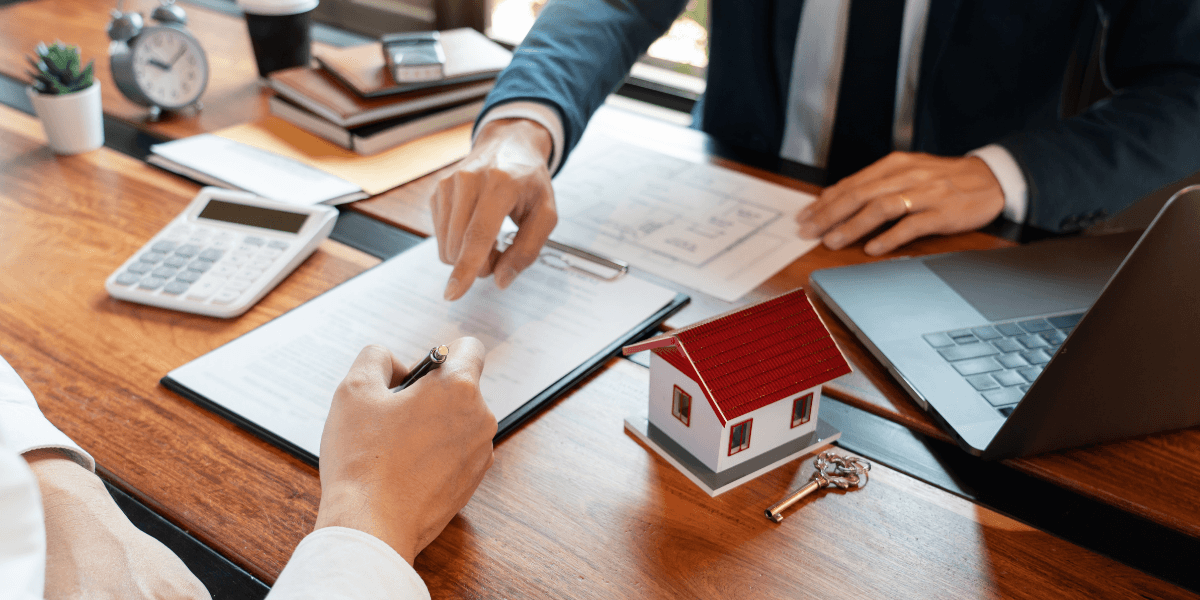 Two businesspeople discussing paperwork with a miniature house and calculator on the table
