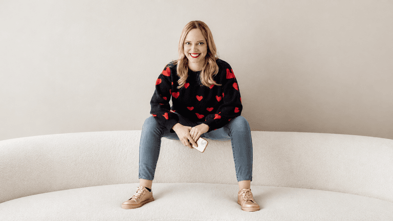 Woman with long blonde hair in a heart-patterned sweater sitting on a couch