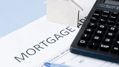 Mortgage application form, calculator, silver house model, and blue pen on a table