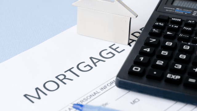Mortgage application form, calculator, silver house model, and blue pen on a table