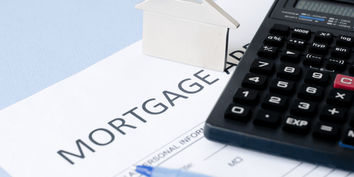 Mortgage application form, calculator, silver house model, and blue pen on a table