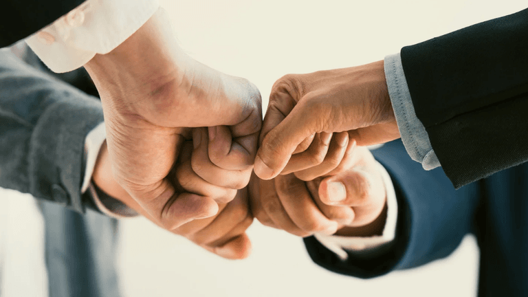 Four hands performing a fist bump, symbolizing teamwork and collaboration