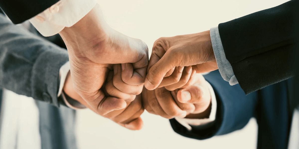 Four hands performing a fist bump, symbolizing teamwork and collaboration
