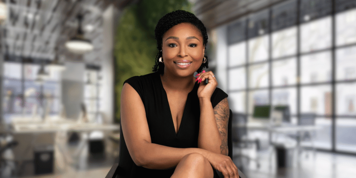 Smiling woman in black dress seated confidently in modern office setting.