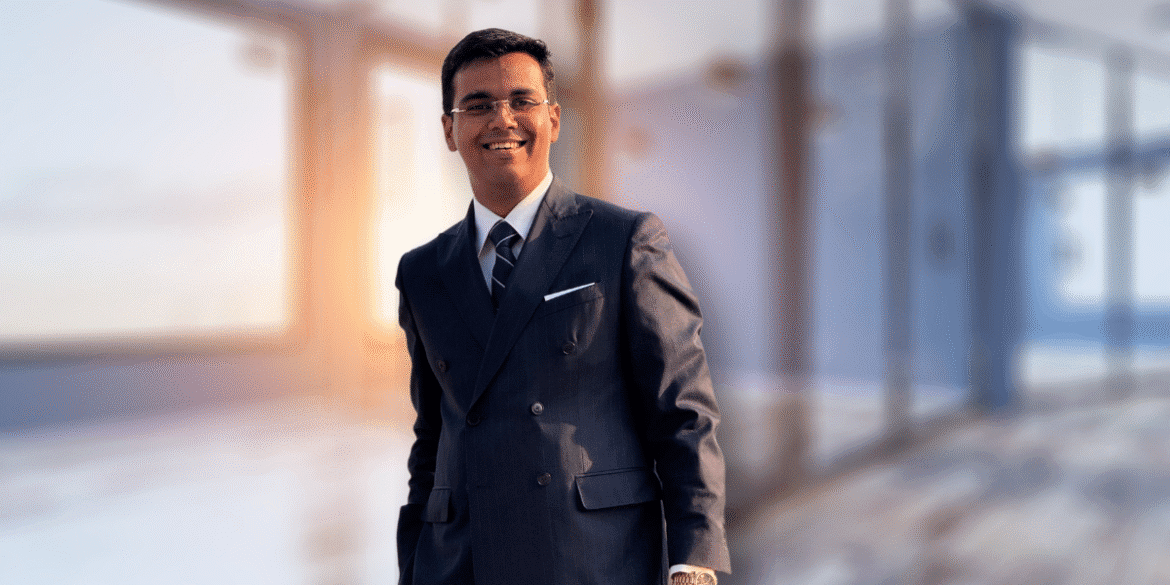 The image features Vibhaas Singh, the visionary behind Hemco, wearing a formal suit and standing confidently in a modern office setting, symbolizing innovation and leadership in kitchen technology.