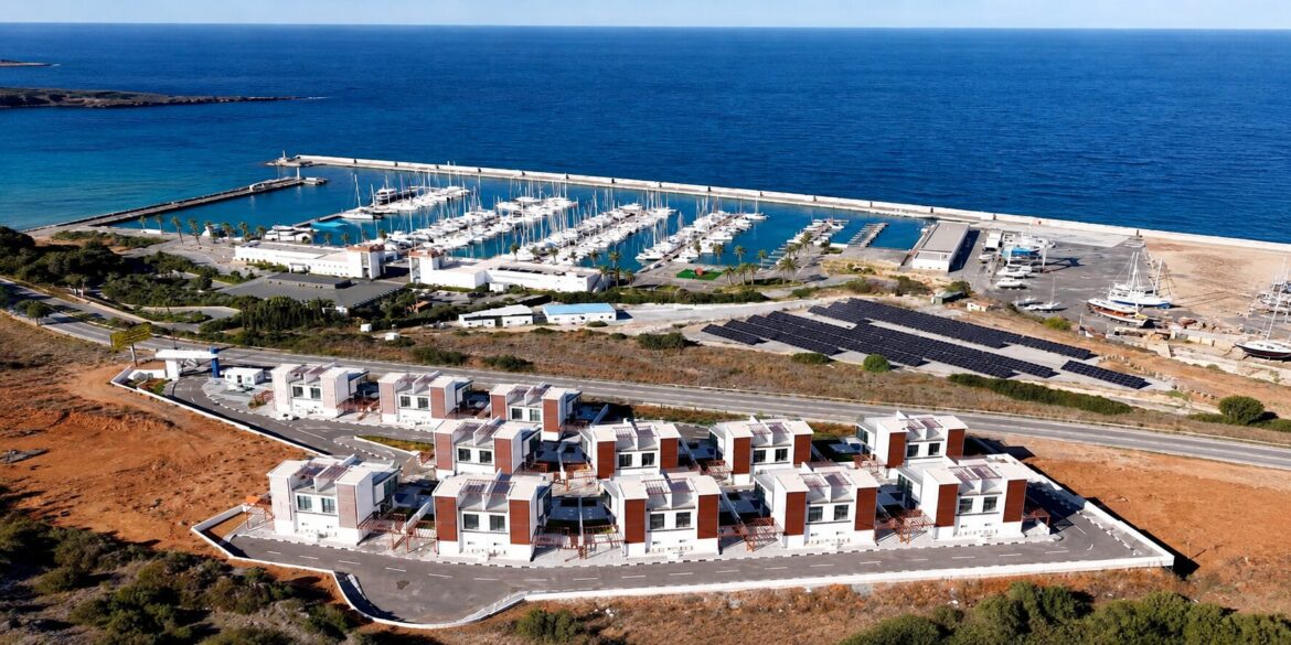 Aerial view of modern coastal homes beside a marina filled with yachts and the Mediterranean Sea.